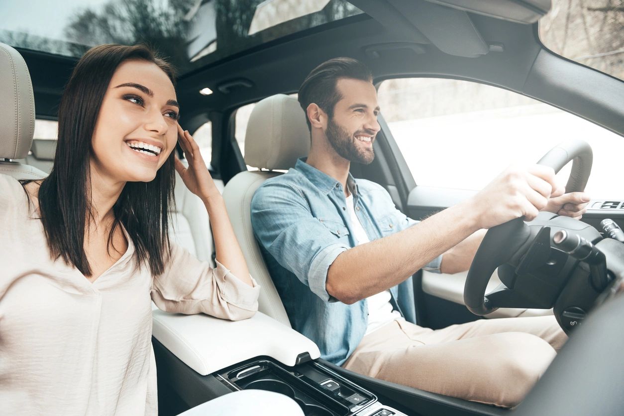 A man and woman sitting in the driver 's seat of a car.