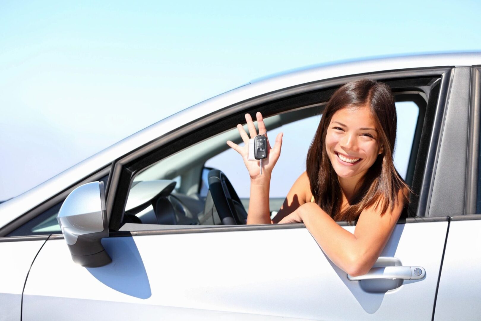 A woman sitting in her car holding up three fingers.